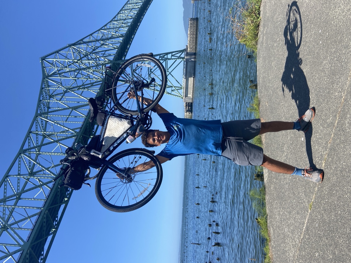 Yusuf holding his bicycle overhead at the Pacific Coast, at the end of his ride across America